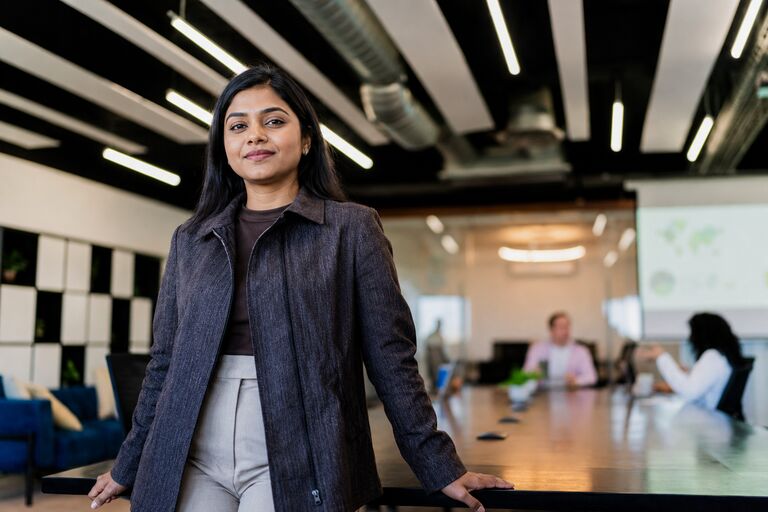 A professional in a meeting room with colleagues working behind her